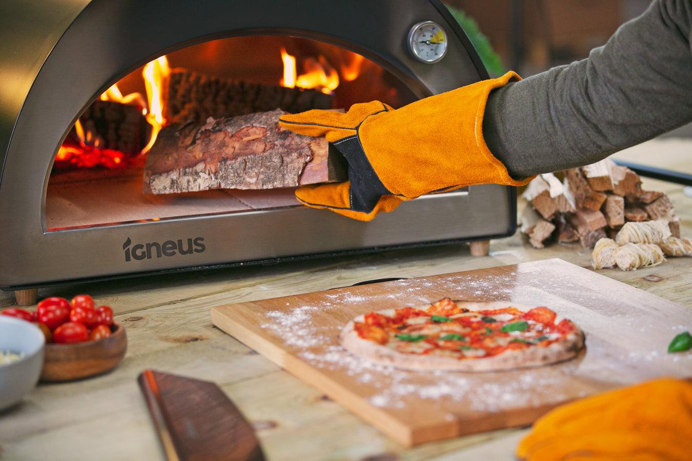 person adding log to wood fired pizza oven